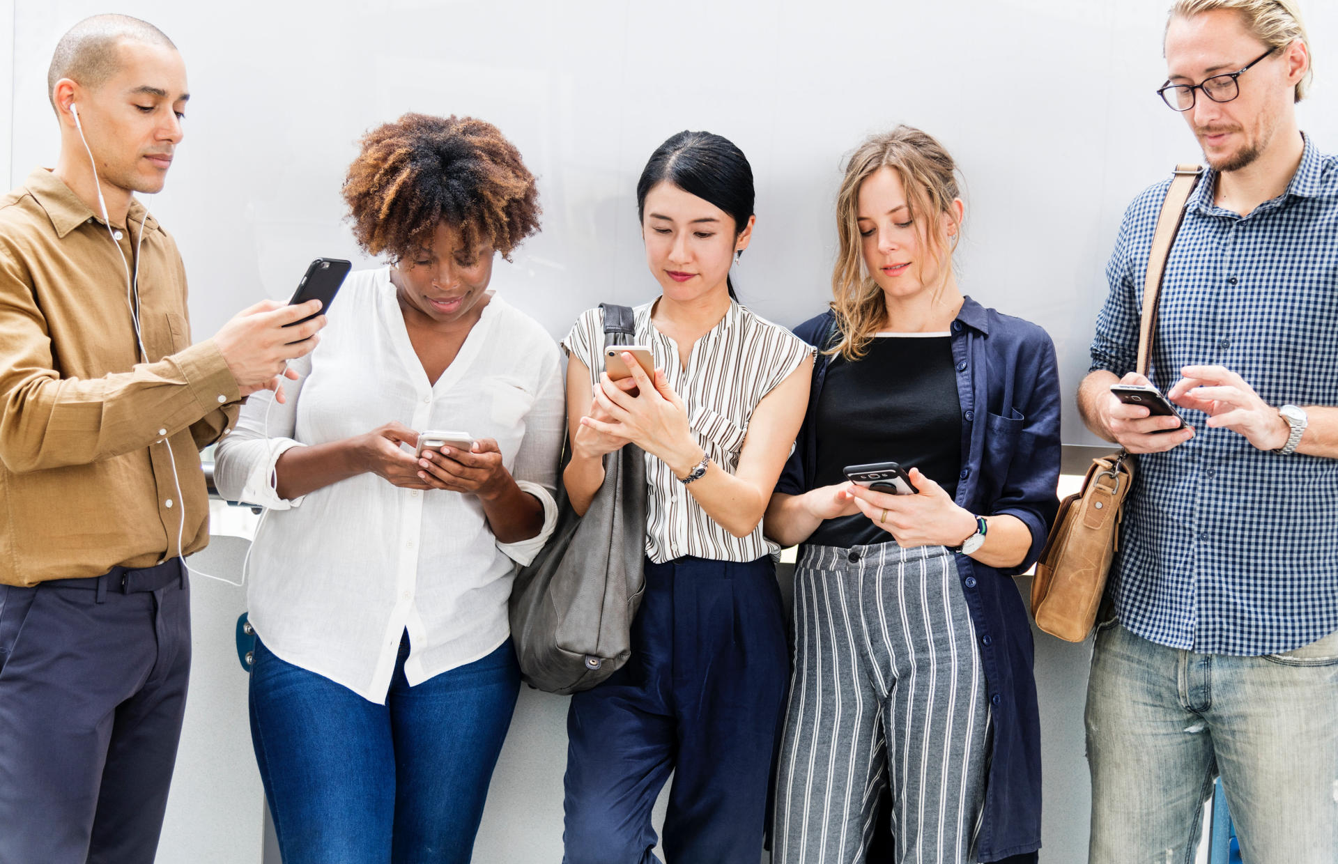 A group of people stand together and look at their phones.