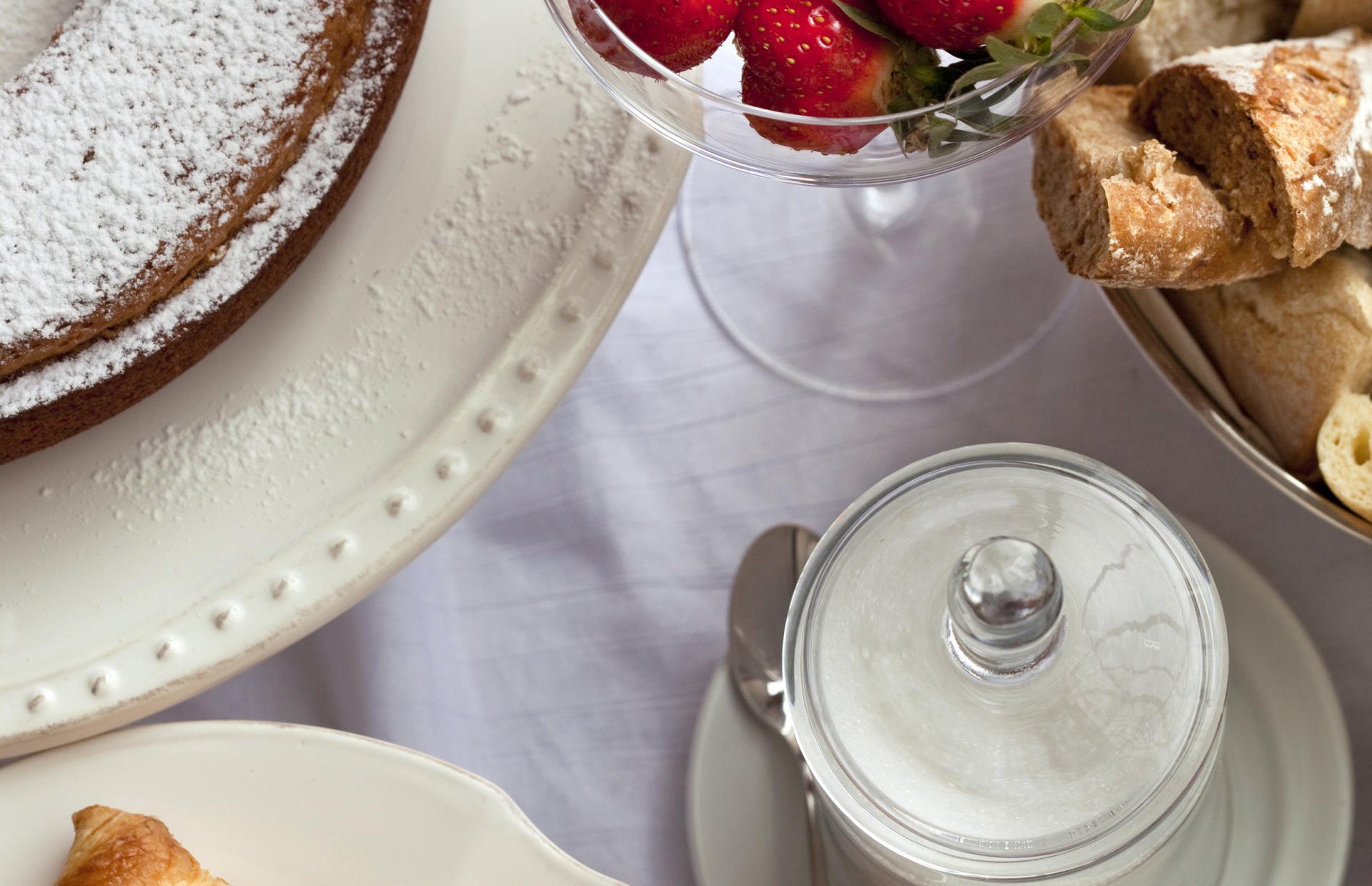 Plates of cake, bread, and strawberries sit on a table.