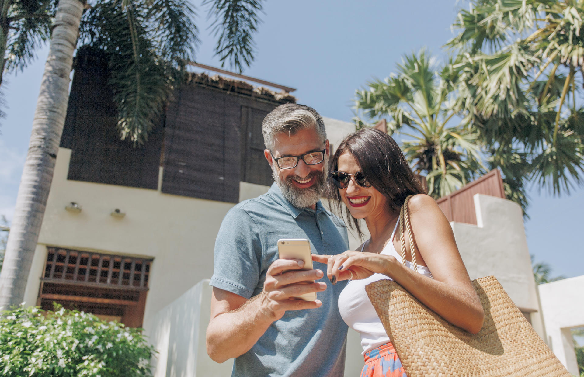 Two hotel guests look at a phone in front of a hotel.