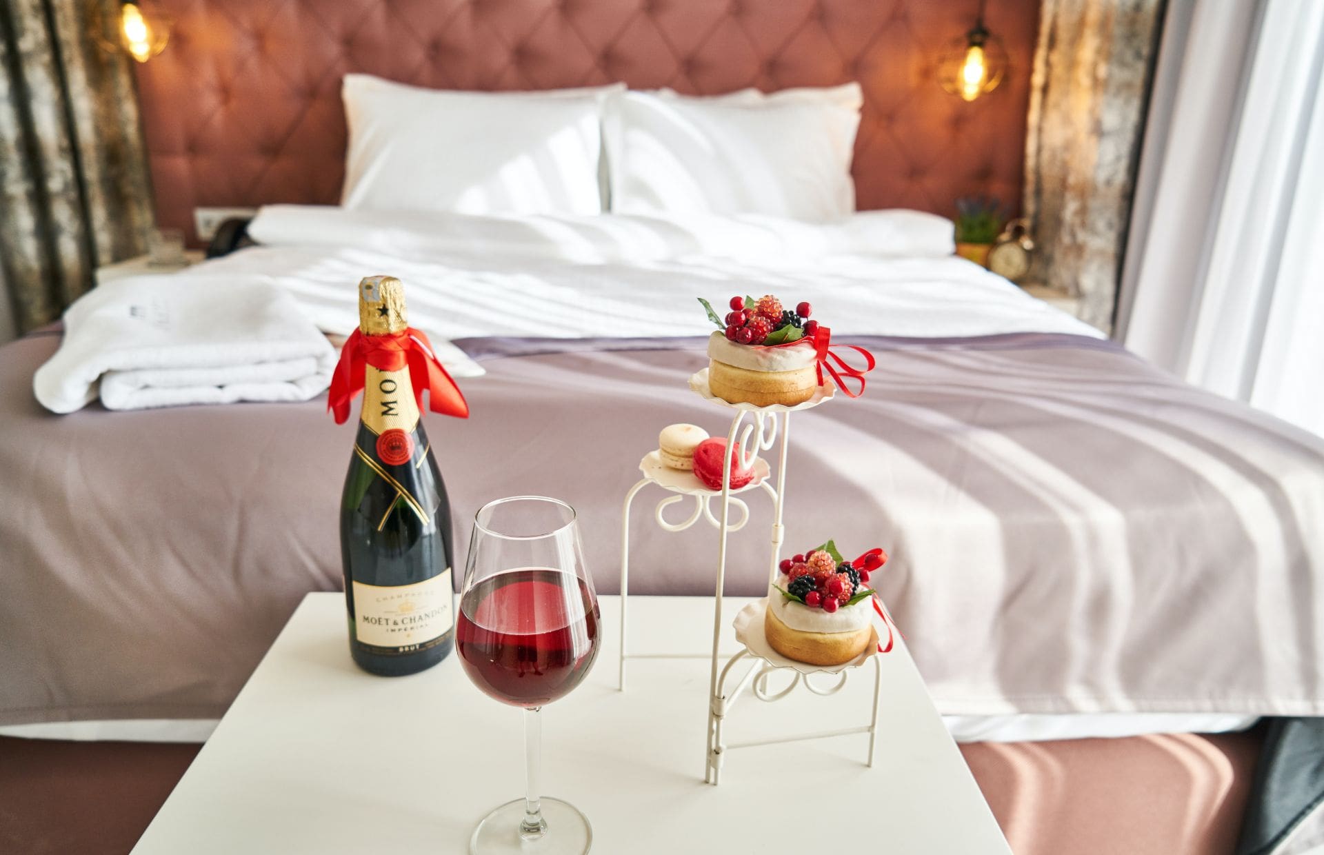 A bottle of wine and trays of desserts sit on a table in a hotel room.