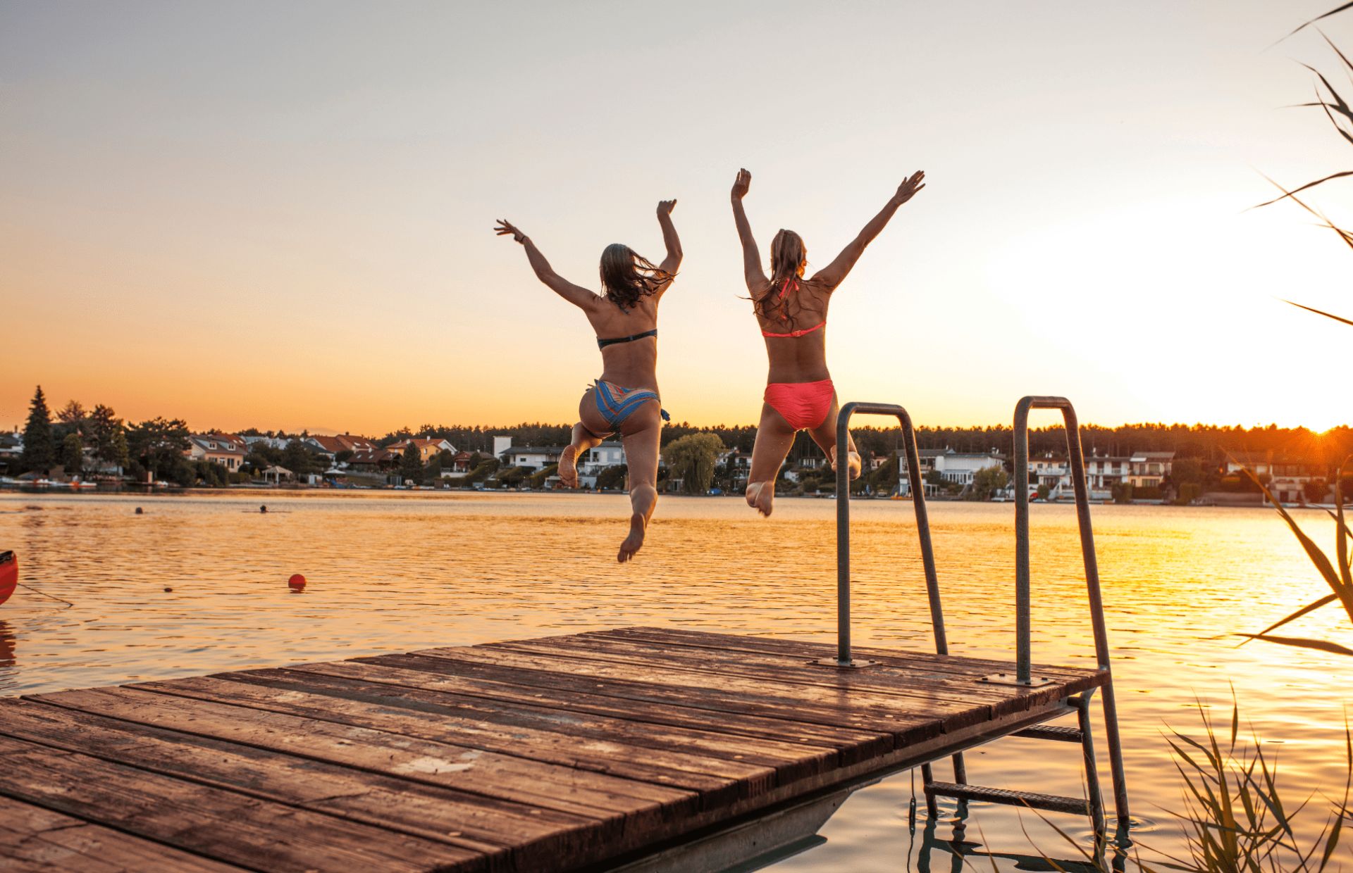 2 women jump into a lake at sunset