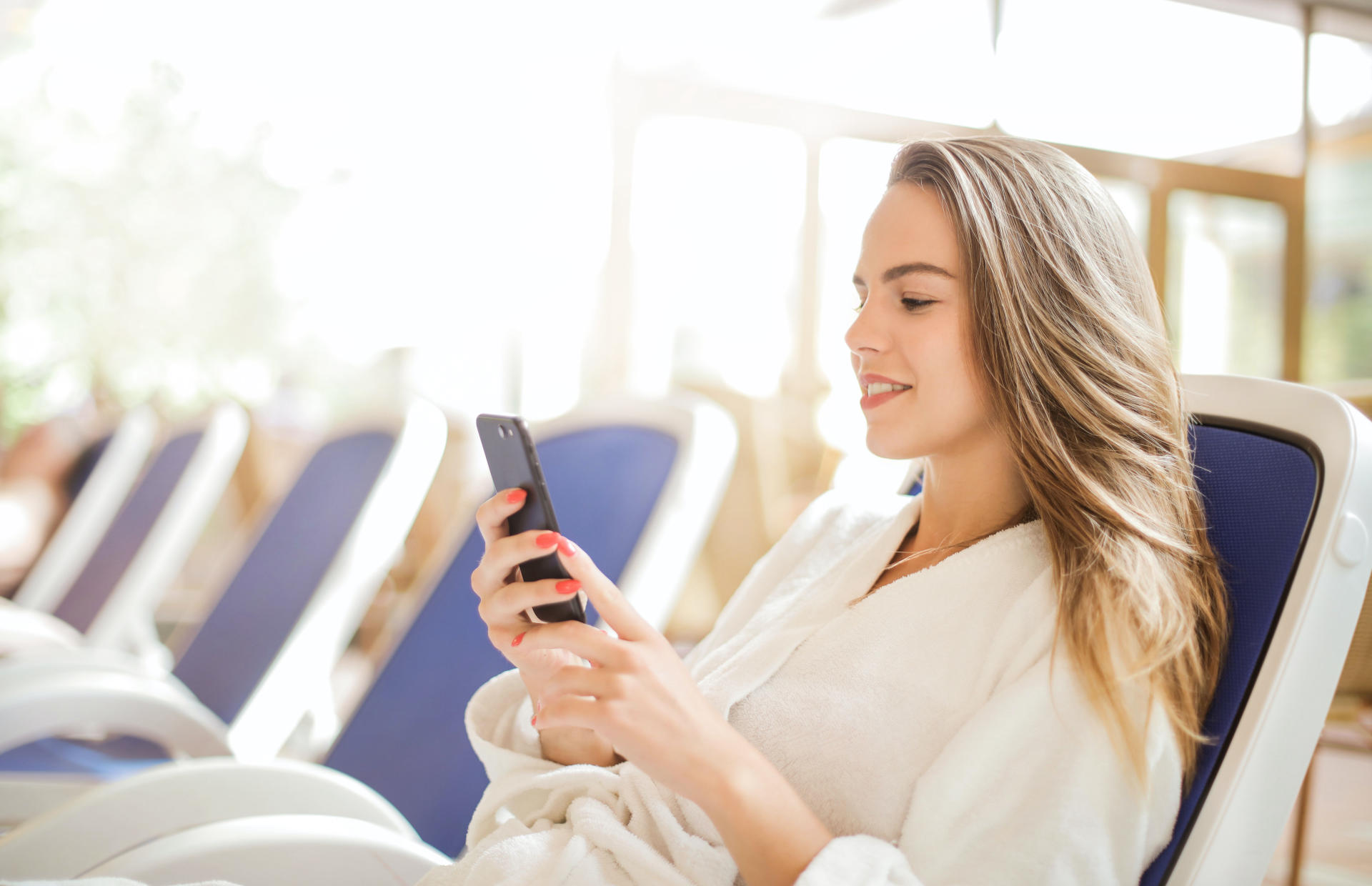 A hotel guest in a robe reclines on a chair and looks at their phone.