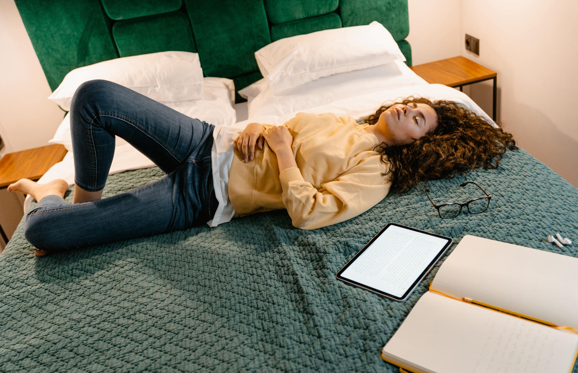 A hotel guest lays on the bed next to their mobile device.