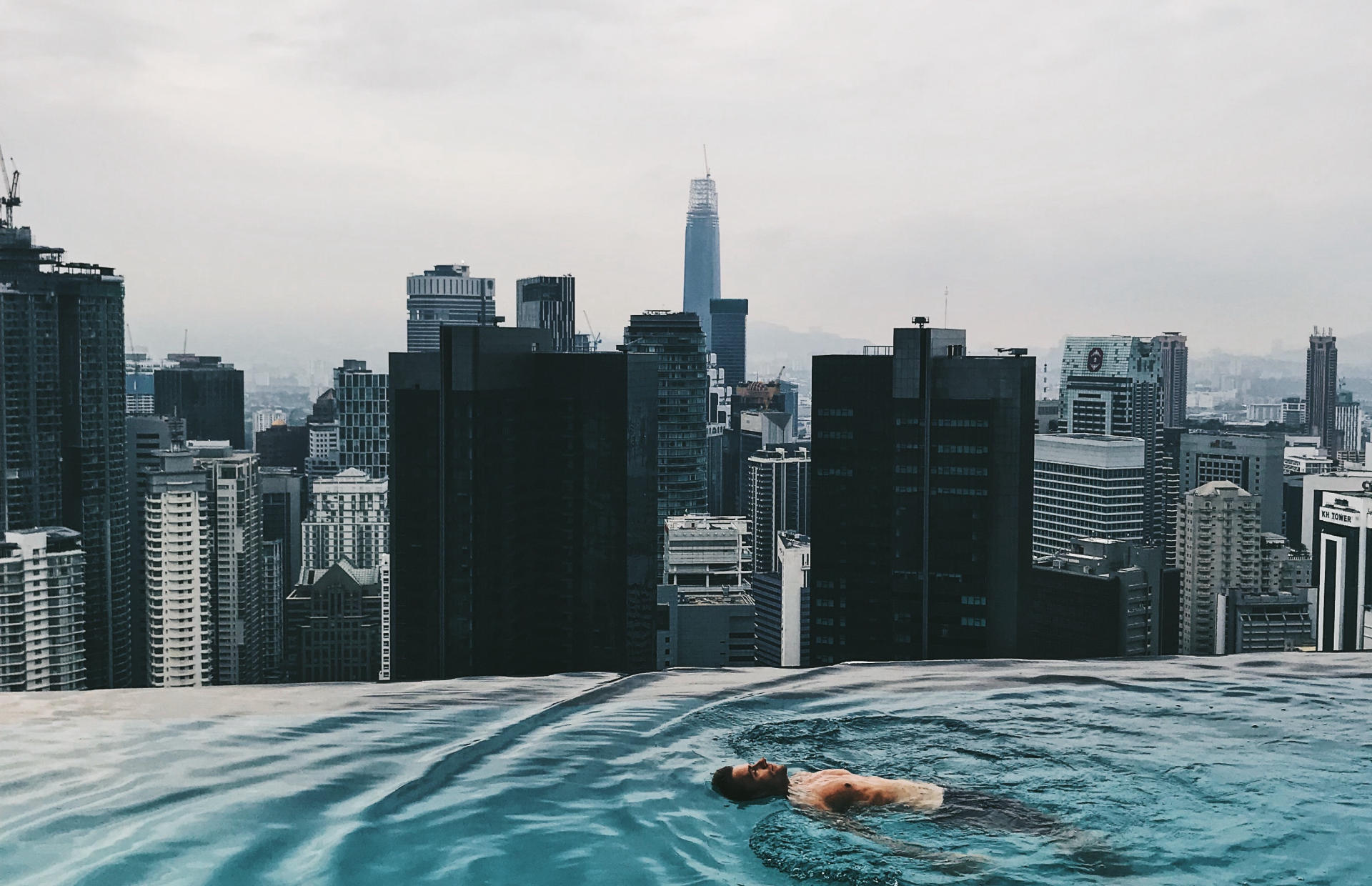 A man swims at the edge of a pool that overlooks a city.