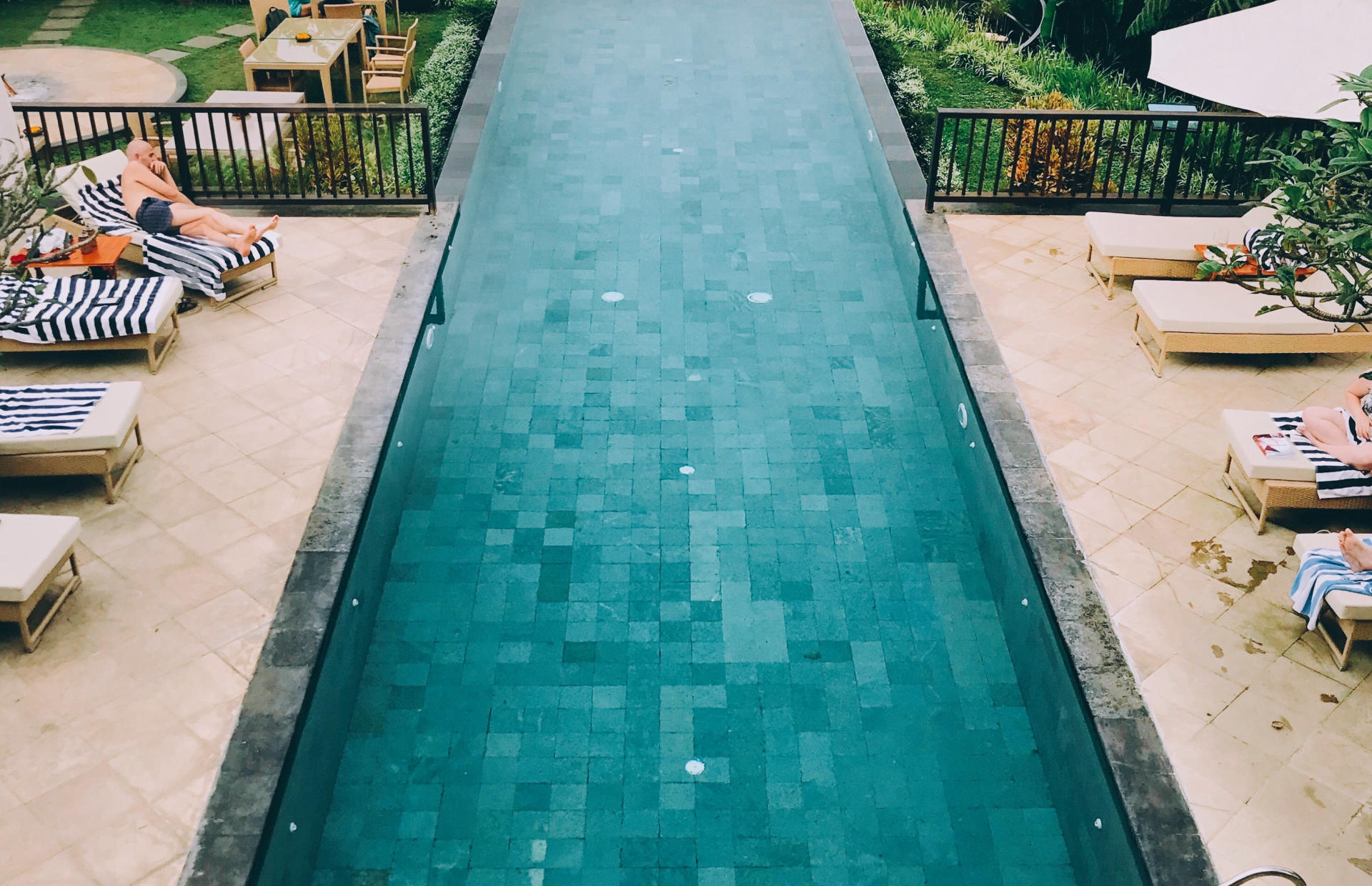 An aerial view of a hotel pool shows guests relaxing in pool chairs.