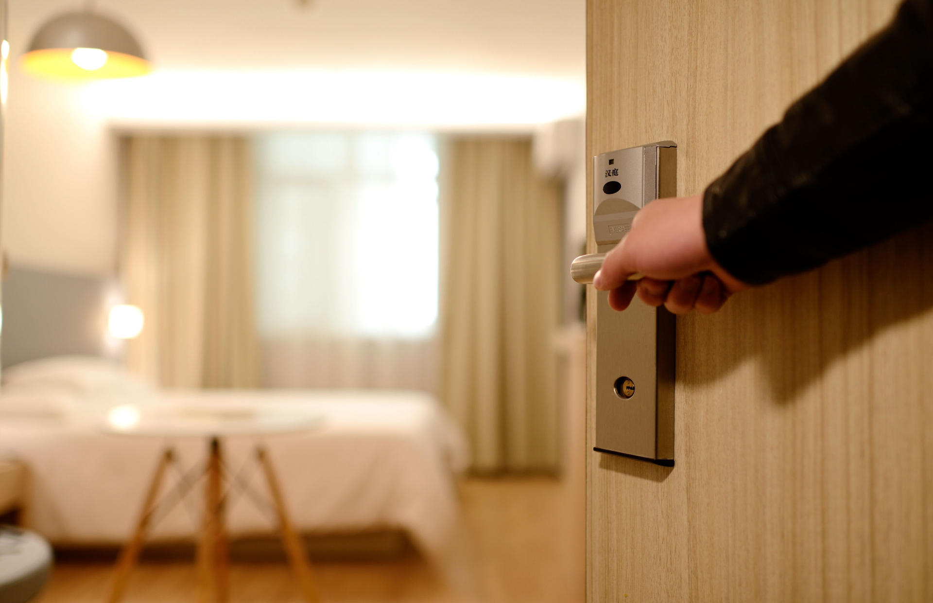 A hotel room door is opened to reveal a bed and window.