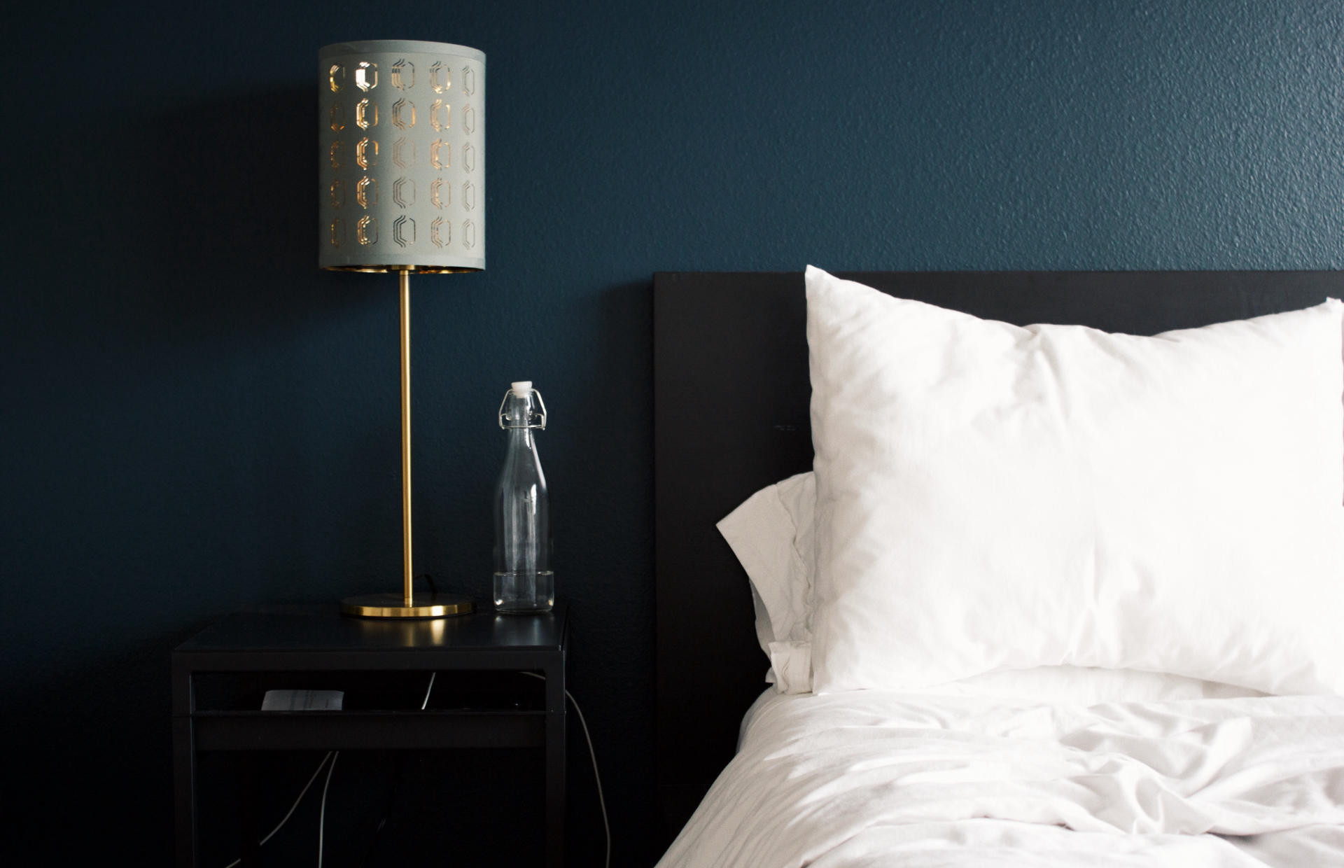 A white hotel bed next to a nightstand with a lamp.