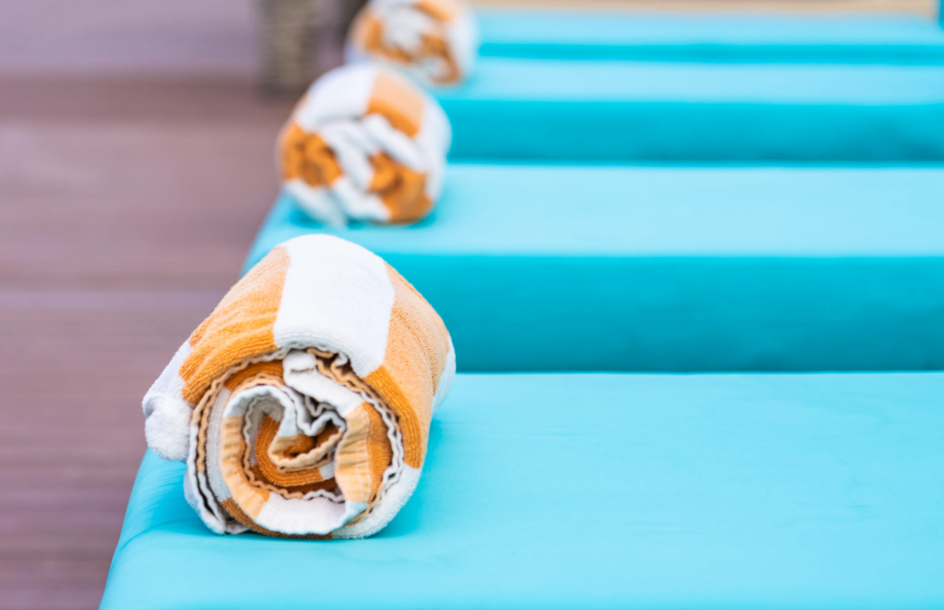 There are four blue pool chairs with striped rolled-up towels.