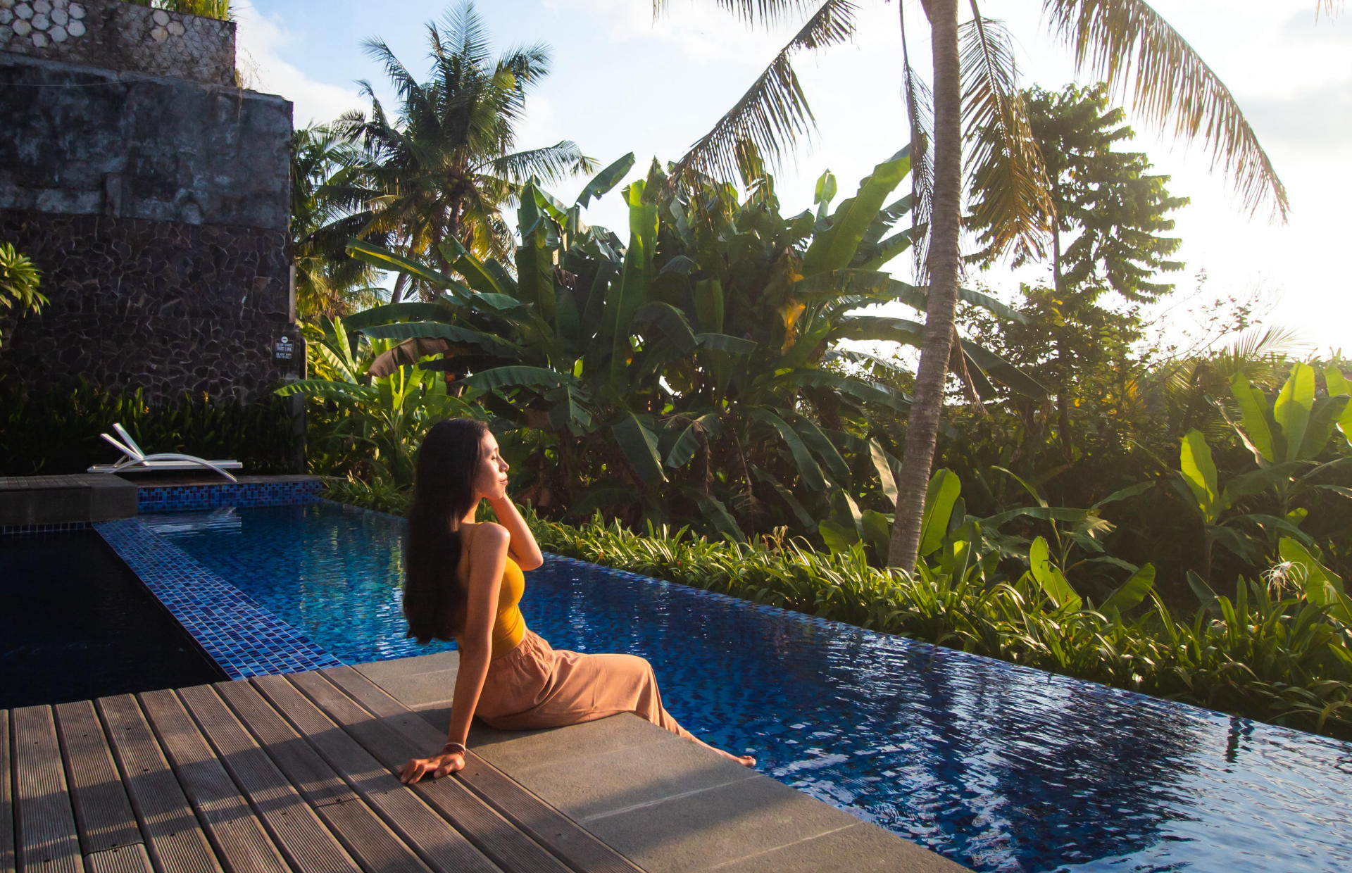 A woman is sitting on the edge of a hotel pool.