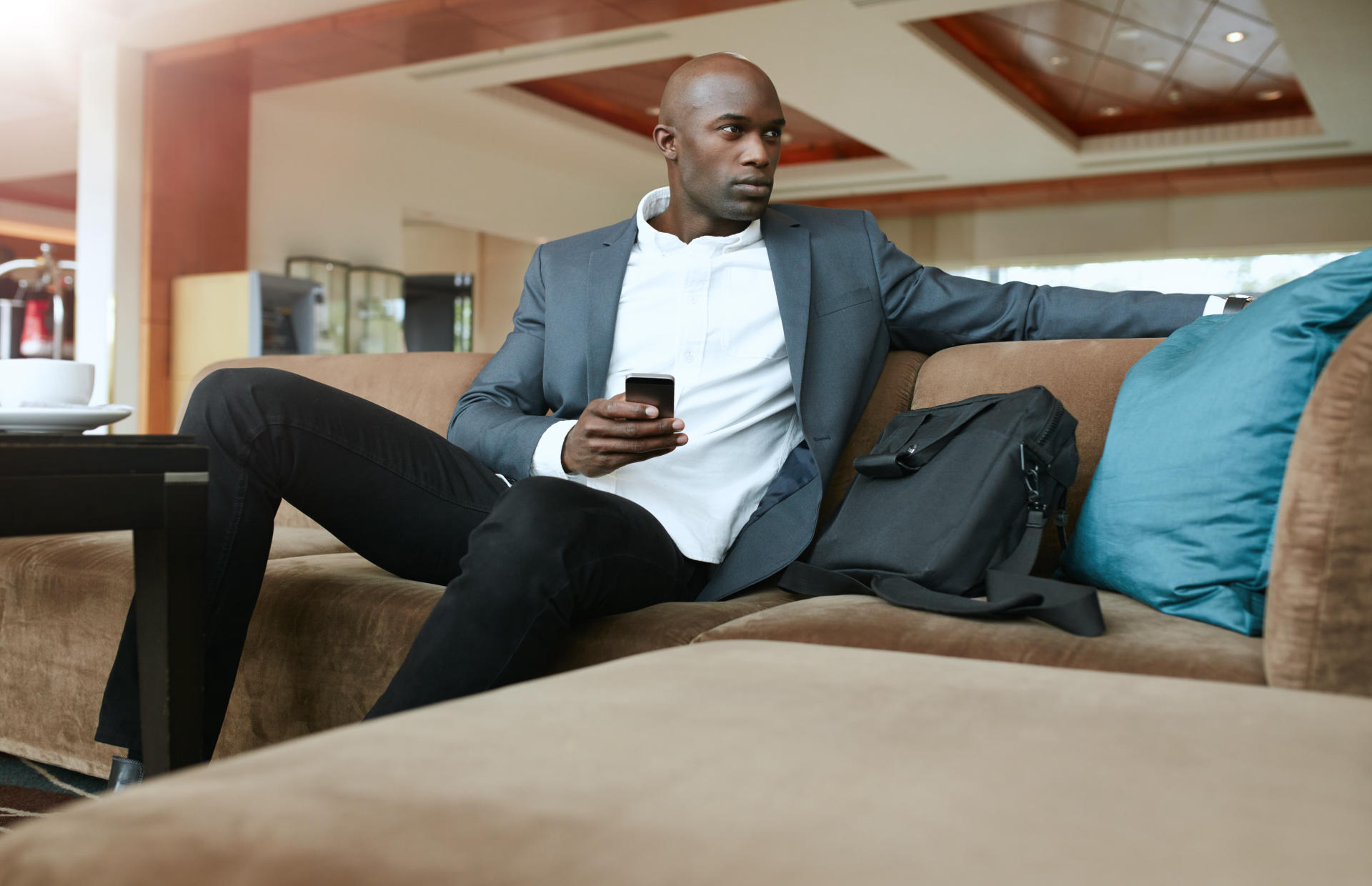 A business man is sitting on a couch in a hotel lobby with his phone in his hand.