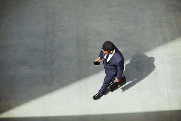 Man walking holding cell phone and briefcase.